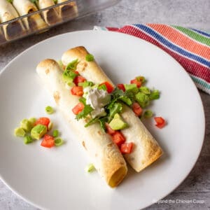Two flautas topped with fresh tomatoes and herbs.