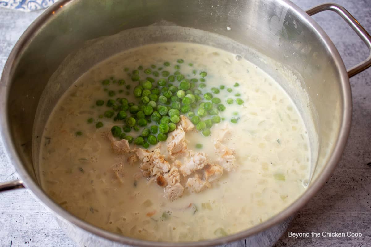Chicken and frozen peas in a pot of soup.