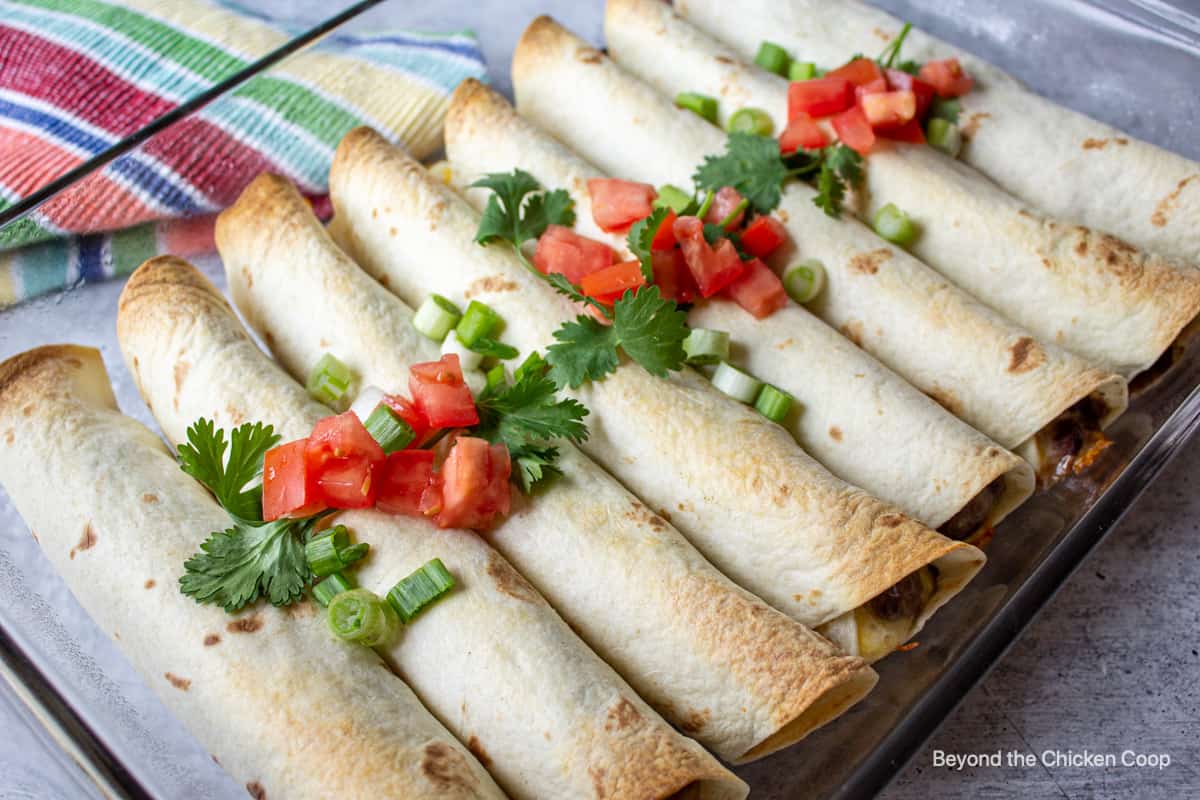 A casserole dish with rolled tortillas and fresh tomatoes and cilantro.