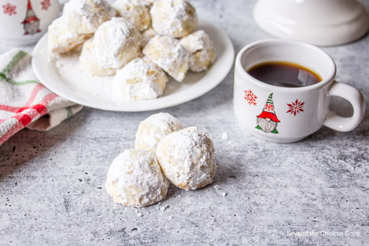 Three snowball cookies next to a small mug of coffee.