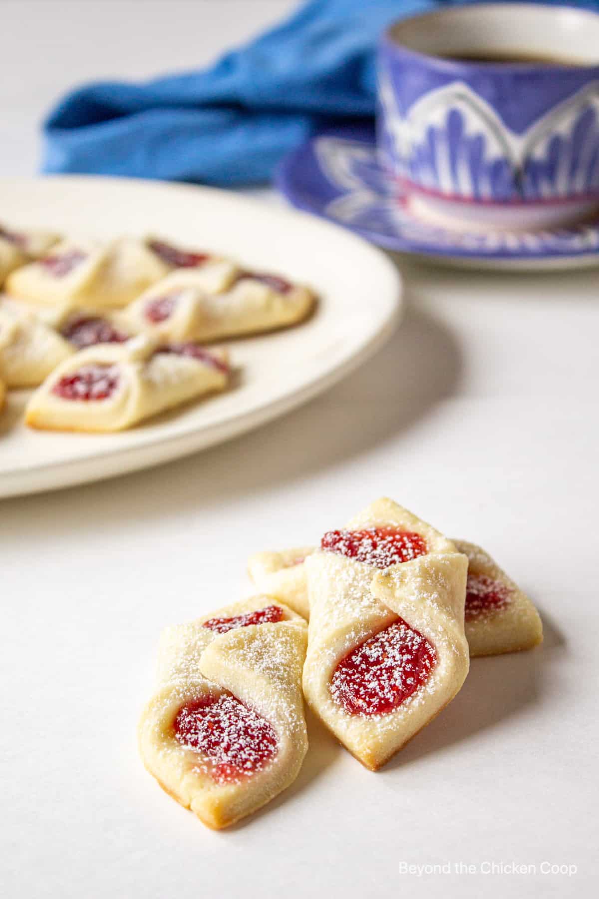 Three jam filled cookies next to a plate of cookies. 