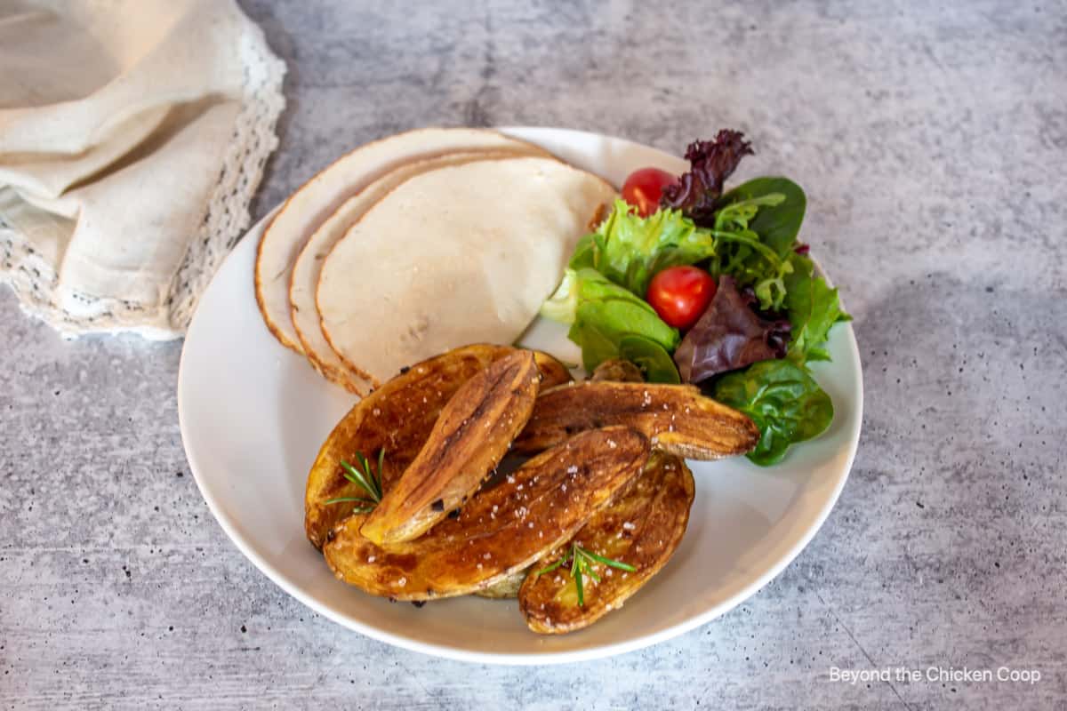 A dinner plate with turkey, roasted potatoes and a green salad.