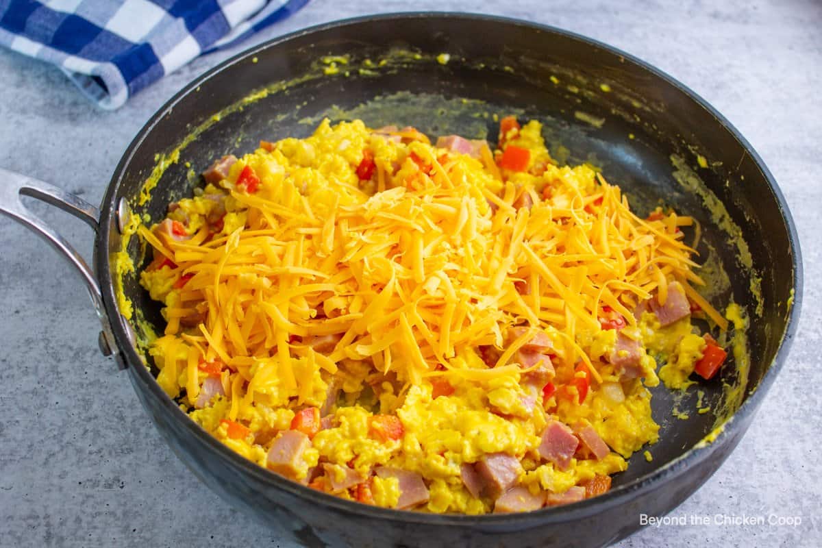Adding cheddar cheese to a pan full of scrambled eggs. 