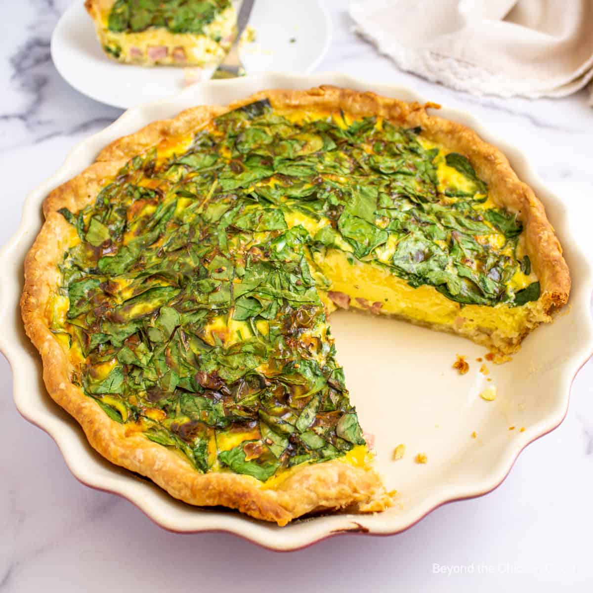 Quiche with spinach and ham with a slice cut out of the quiche.