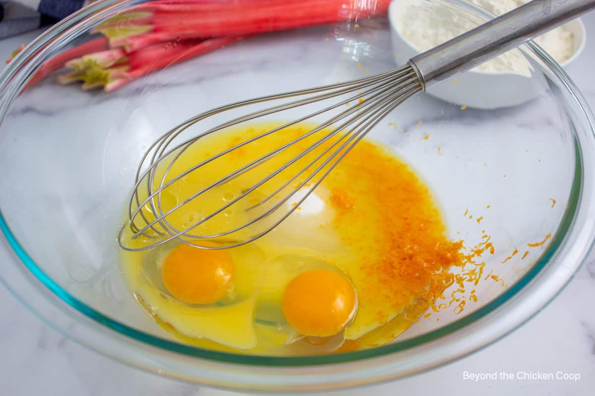 Eggs with sugar and orange zest in a bowl.