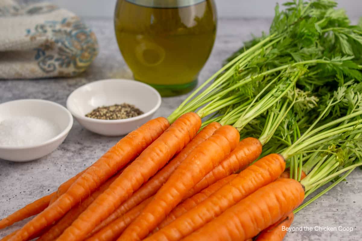 Fresh carrots, olive oil and salt and pepper on a counter.