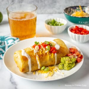 A chimichanga topped with sour cream, tomatoes and onions.