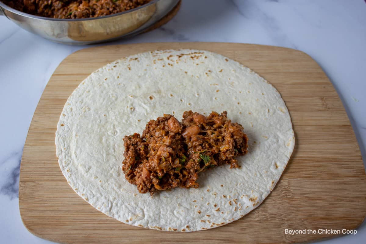 Filling a flour tortilla with ground beef.