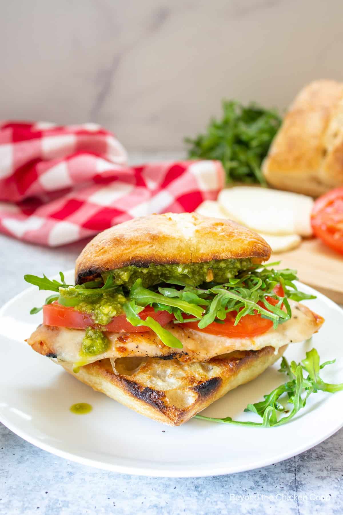 A stacked chicken sandwich with tomatoes and arugula.