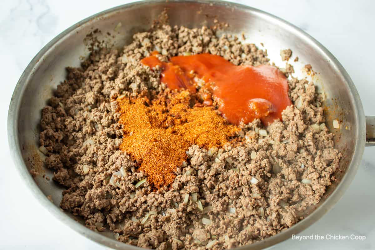 Taco seasoning and tomato sauce added to a pan of ground beef.