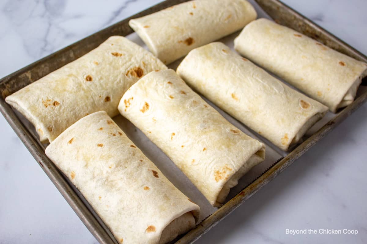 Filled Chimichangas on a baking sheet.