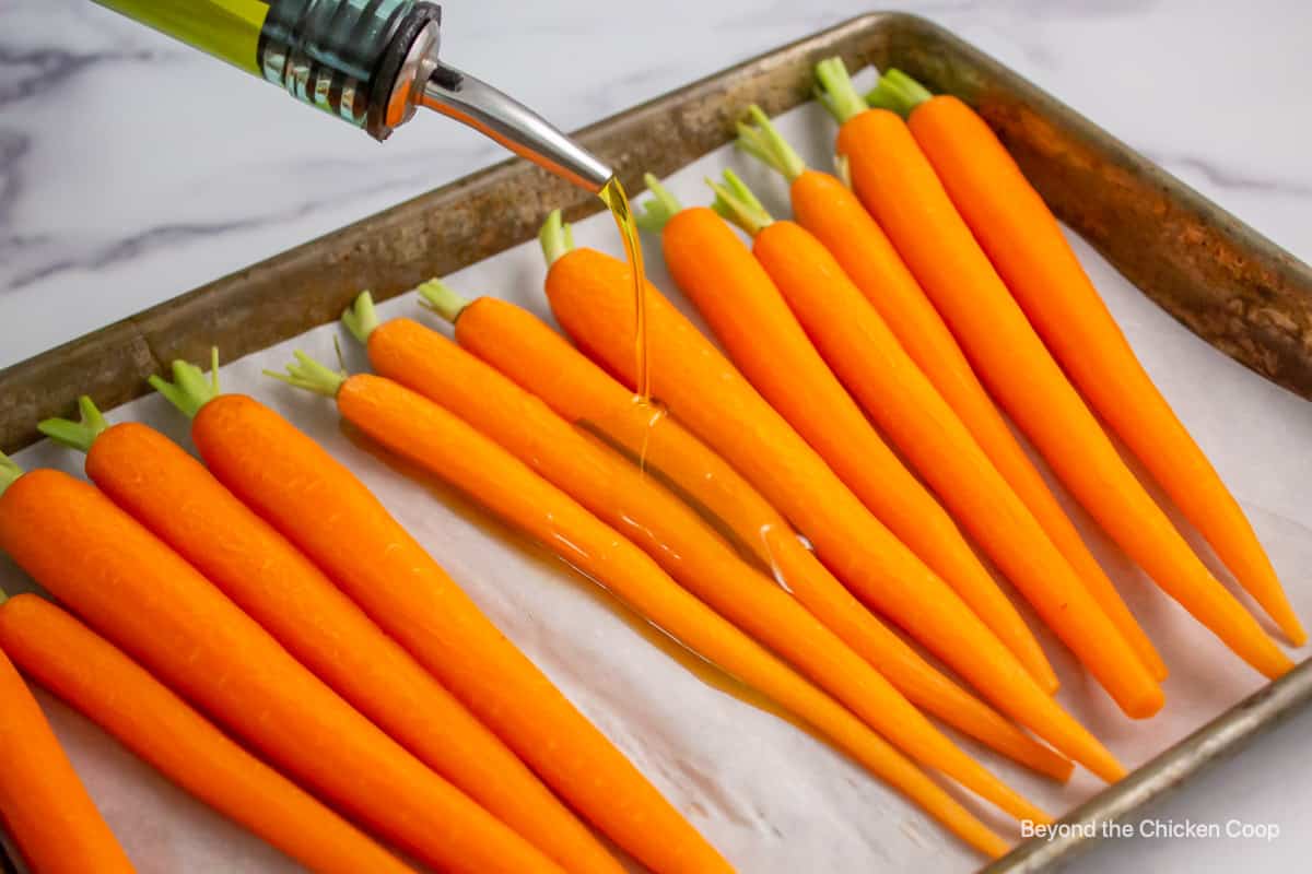 Olive oil being poured over carrots. 