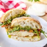 A chicken sandwich on a bun with pesto and arugula.