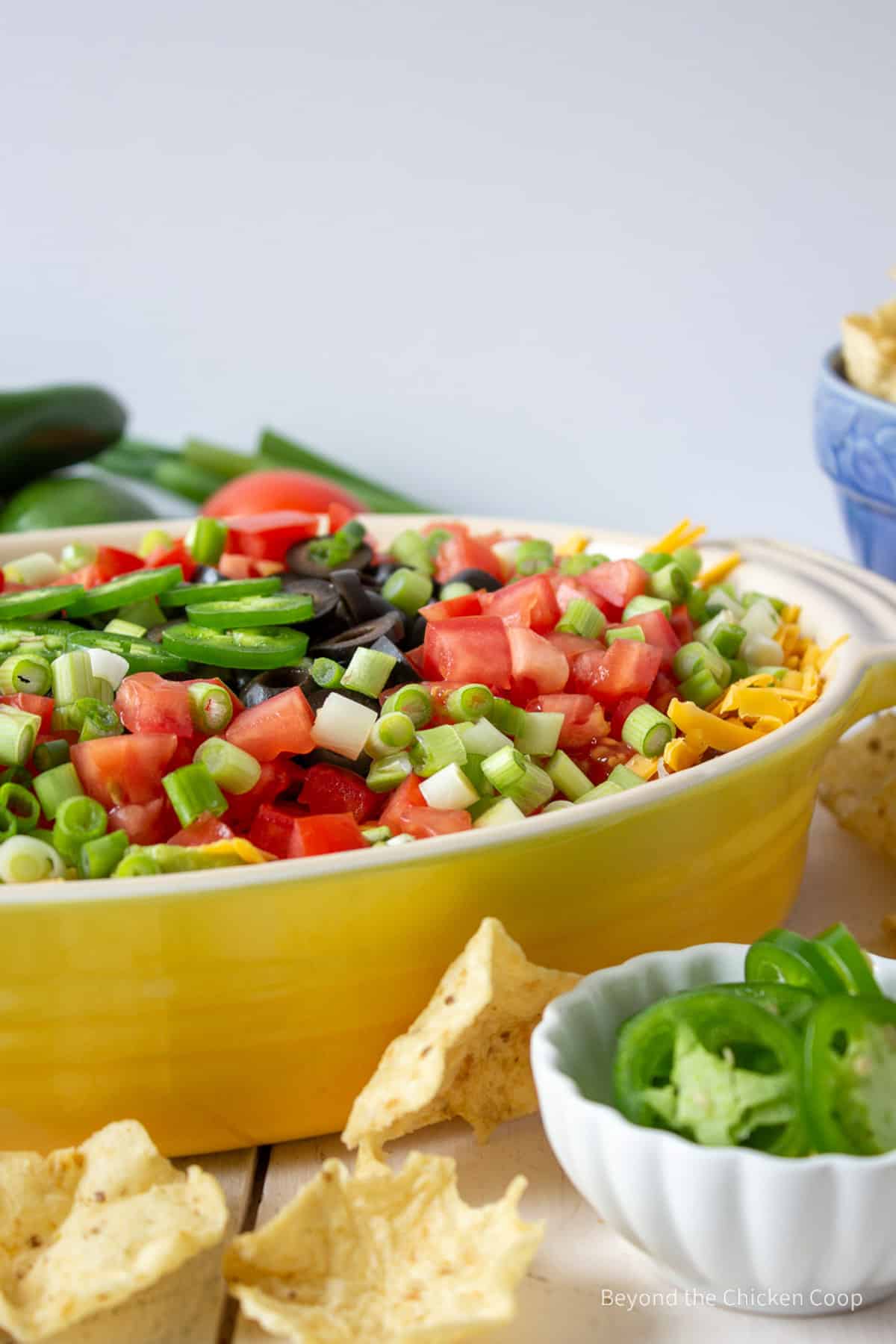 Layer bean dip with tomatoes and onions in a yellow casserole dish.