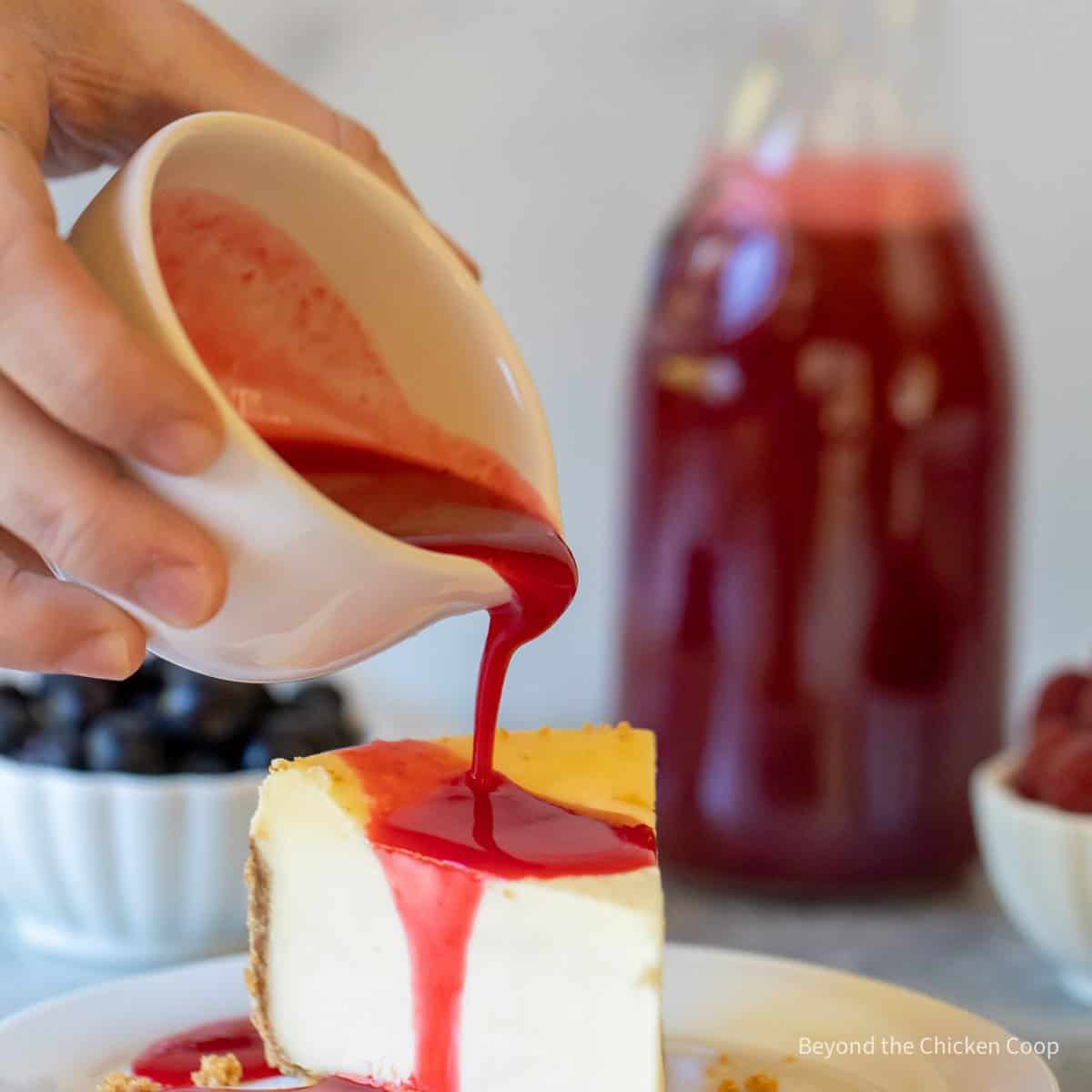 Pouring a red syrup onto a slice of cheesecake.
