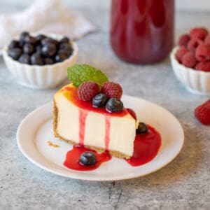 Cheesecake with a red sauce and fruit.