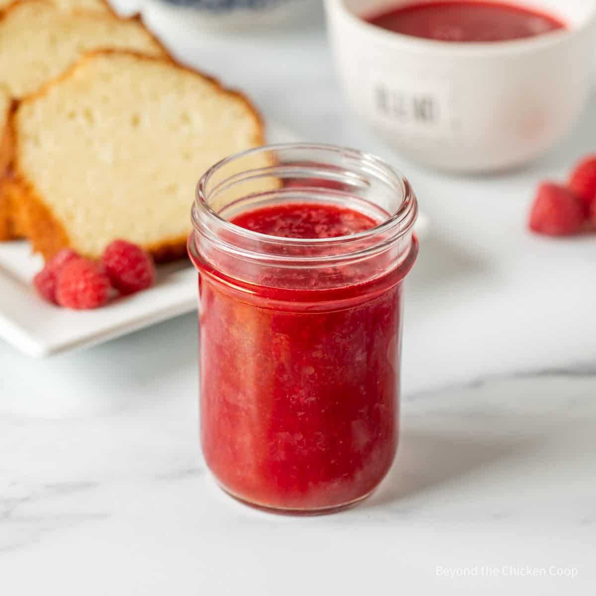 A jar filled with red raspberry sauce.