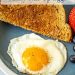 A fried egg on a plate next to a piece of toast.