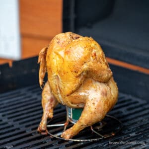 A whole chicken on a can of beer on the grill.