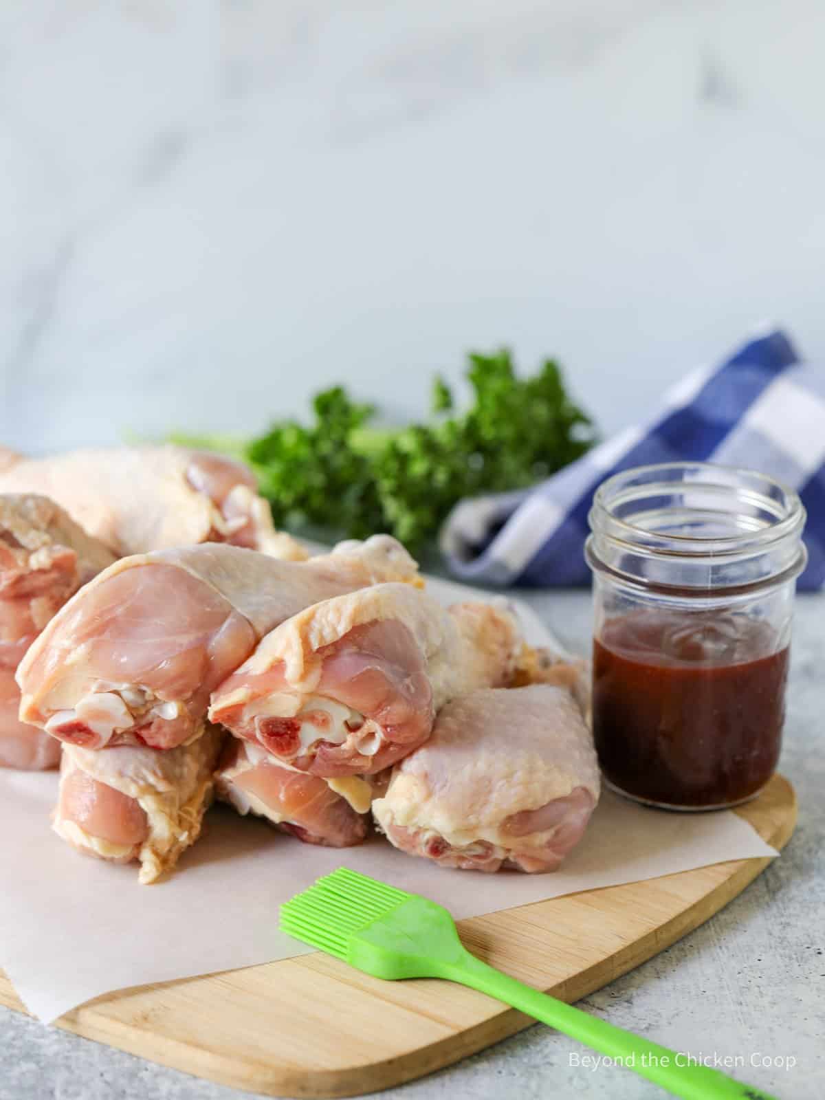 Chicken drumsticks next to a jar of BBQ sauce.