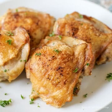 Crispy chicken thighs on a white plate.