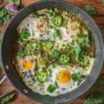 Fried eggs in a pan with cilantro and sliced jalapenos.