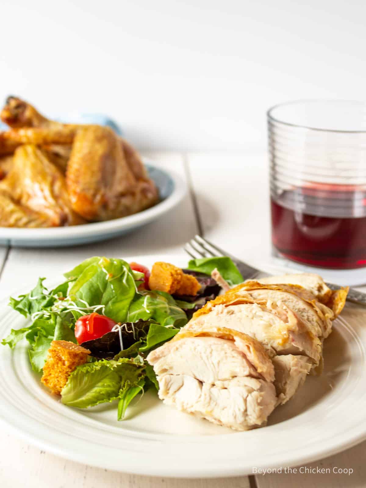 Sliced chicken breast on a plate next to a salad.