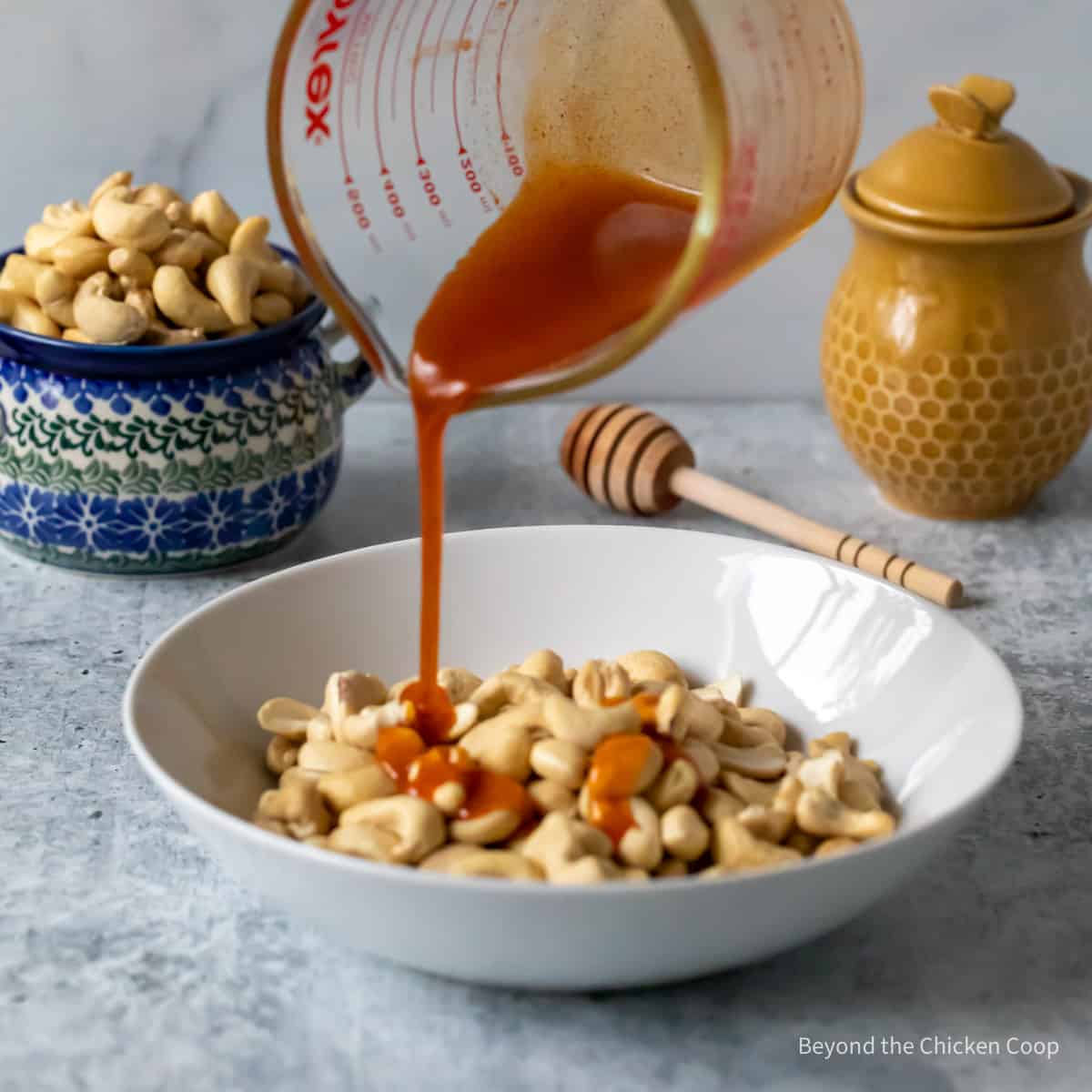 Pouring a honey mixture over cashews.