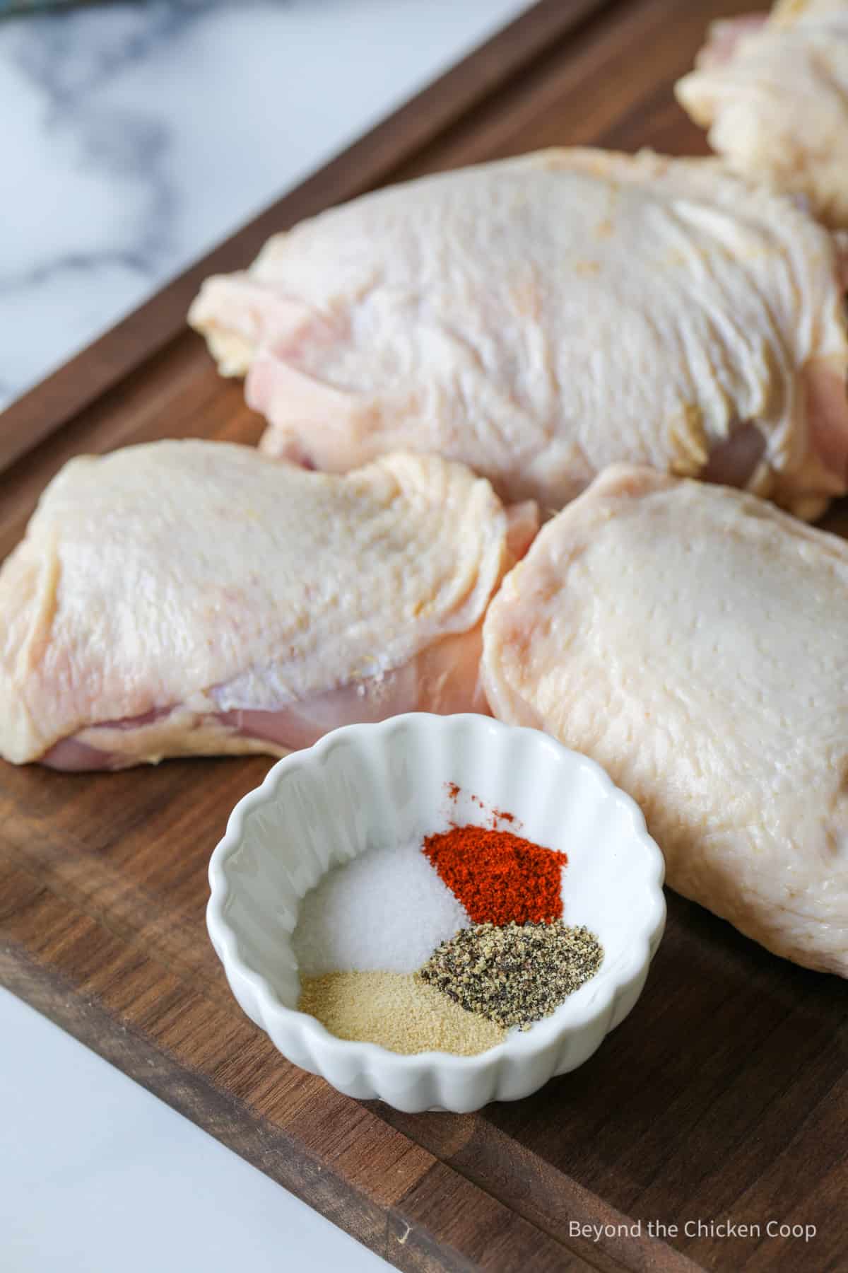 Chicken thighs next to a bowl of seasoning.