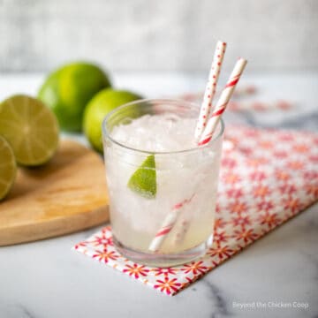 A class of limeade with a lime wedge and two straws.
