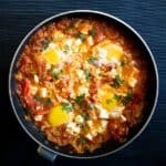 A casserole dish with eggs and cheese in a tomato sauce.