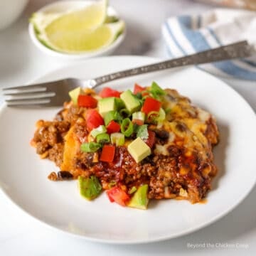 A serving of enchilada casserole topped with tomatoes and avocado.