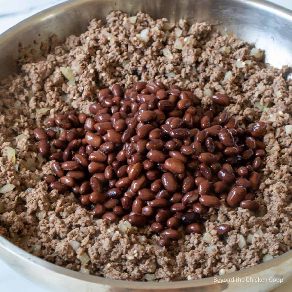 Adding black beans to browned burger.