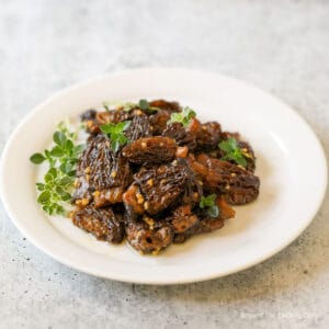 A plate with cooked morels and fresh green herbs.