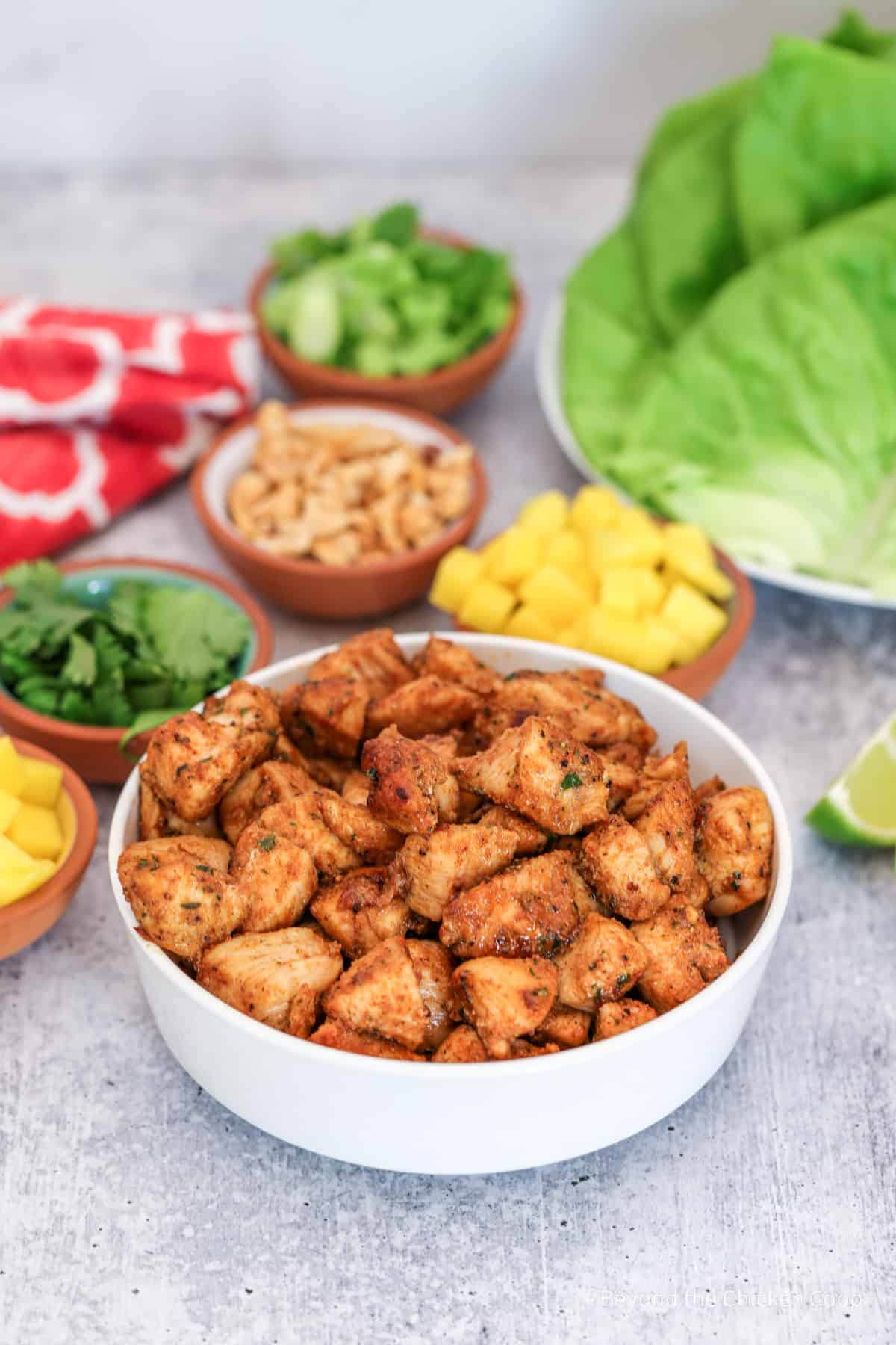 Jerk chicken in a bowl with several smaller sized bowls filled with toppings. 