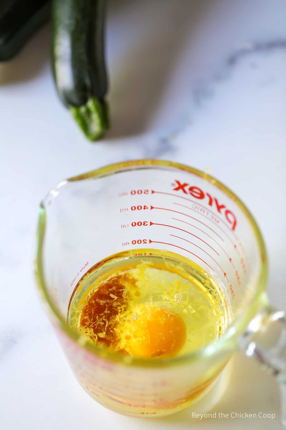 A glass measuring cup with an egg, oil and vanilla.