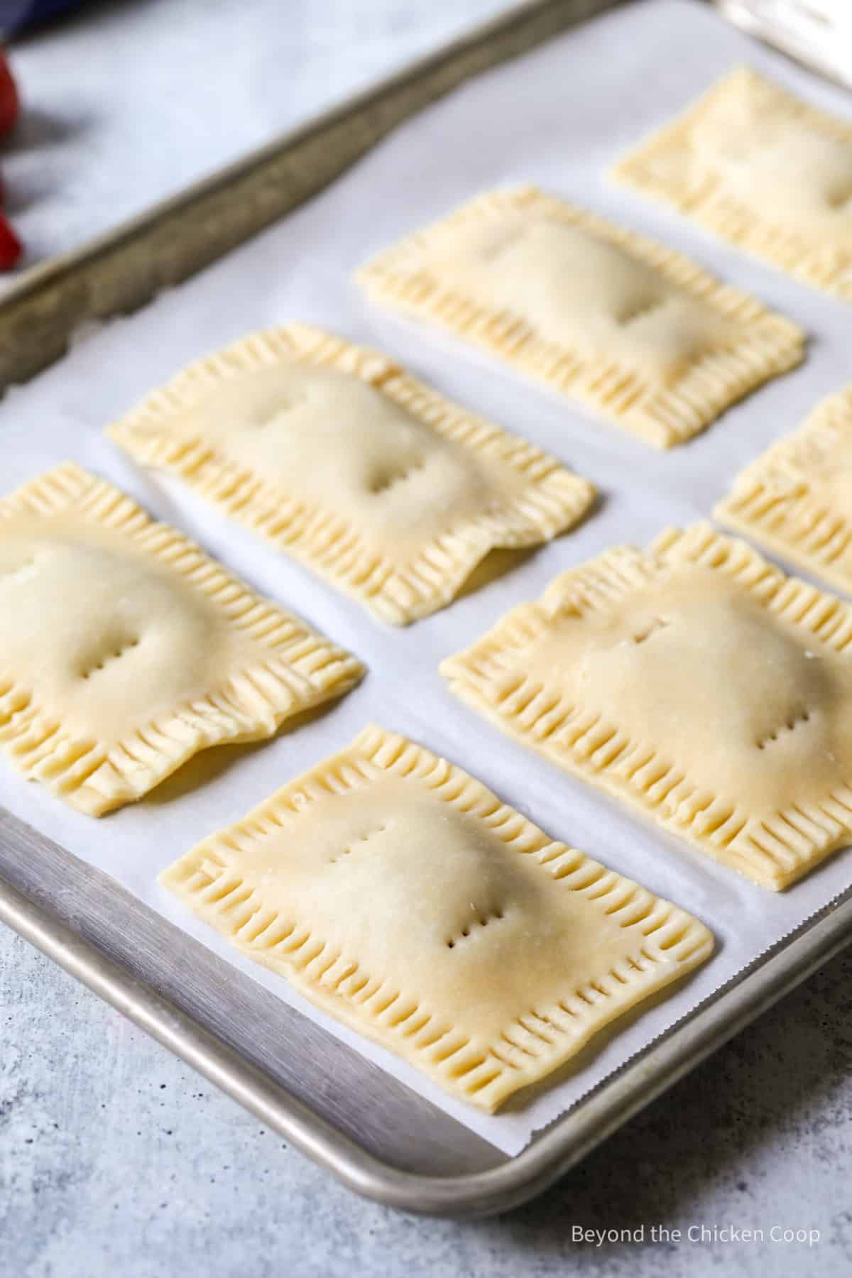 Small unbaked pop tarts on a baking sheet.