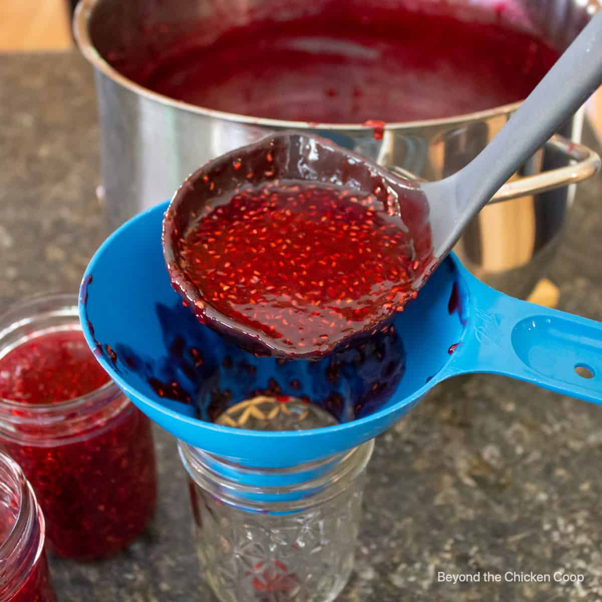 Pouring jam into canning jars using a blue funnel.