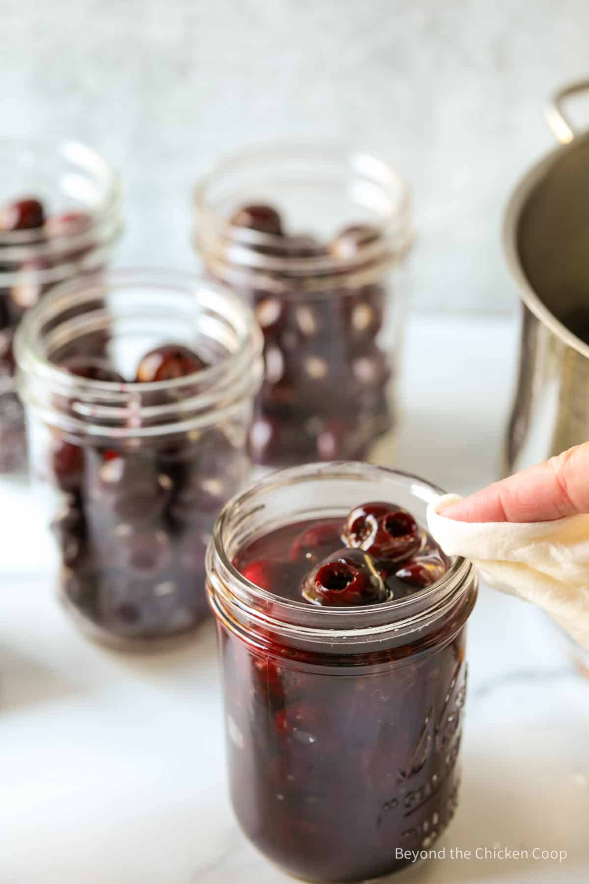 Wiping down the rim of a canning jar filled with cherries. 