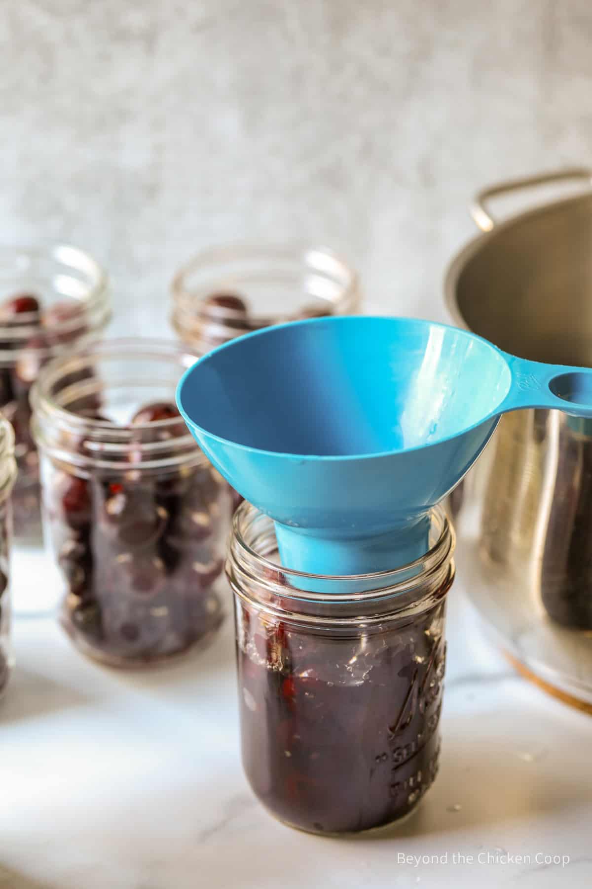 Adding sugar syrup to a jar with cherries using a blue funnel.