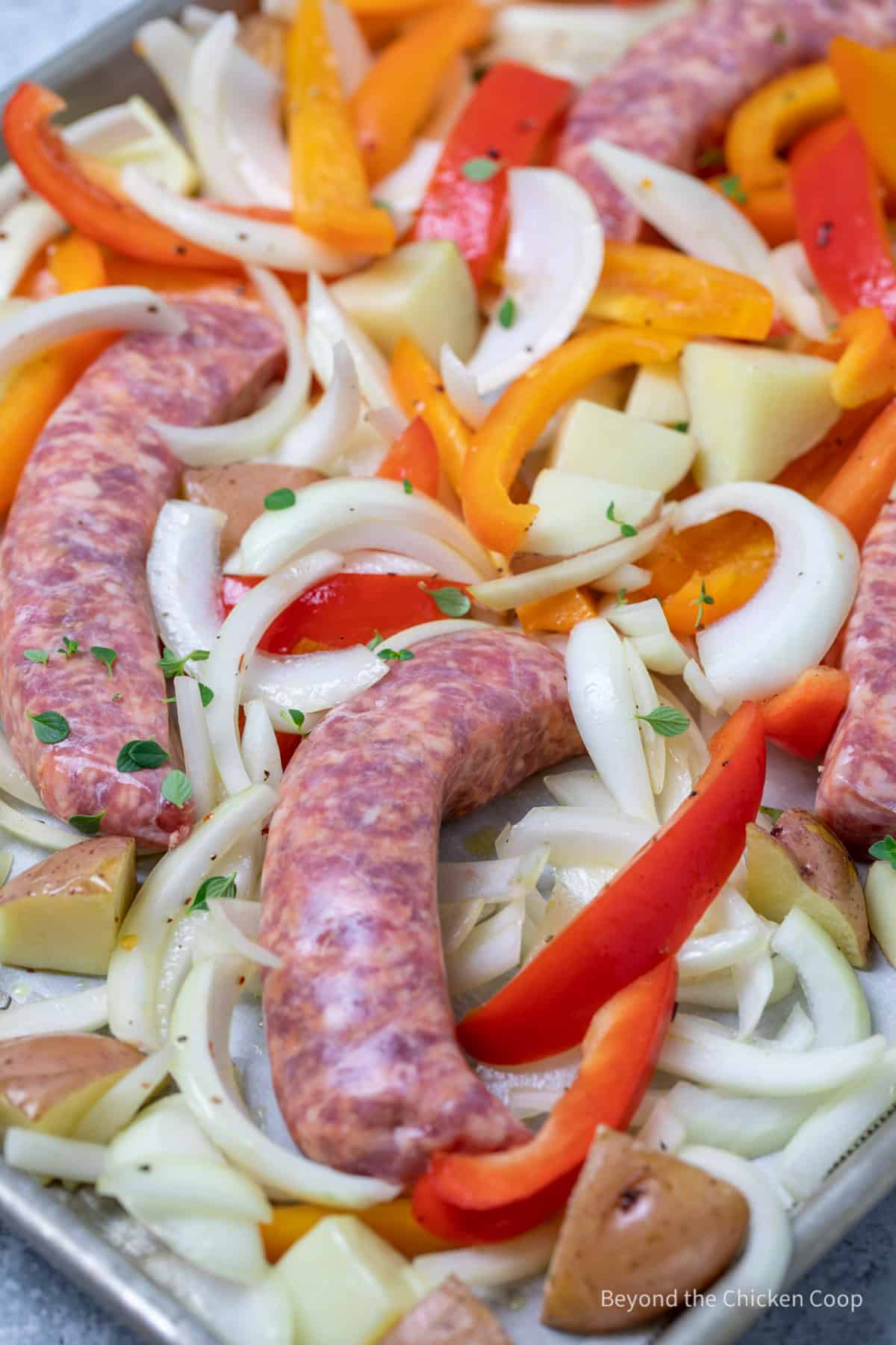 Uncooked sausages with sliced peppers and onions. 