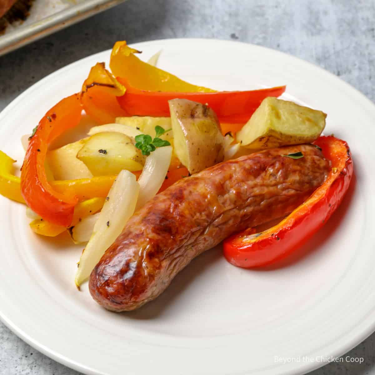 A sausage on a plate with pepper and onion slices.