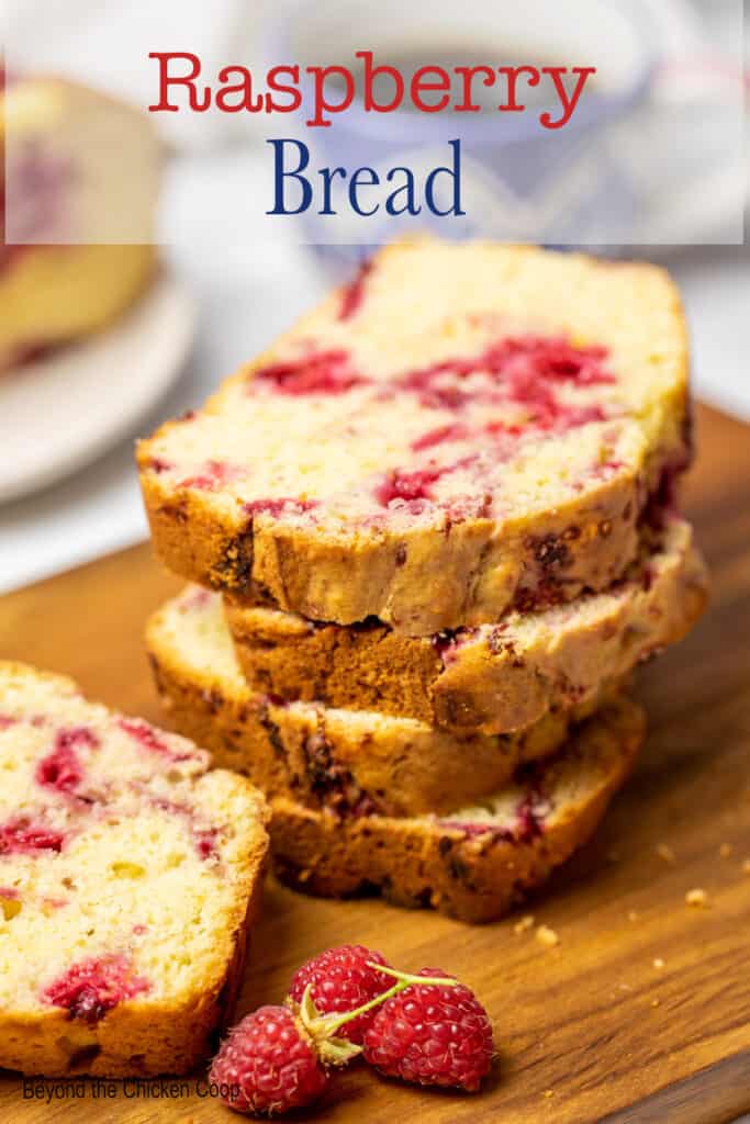 Slices of a breakfast bread with raspberries stacked on a board.
