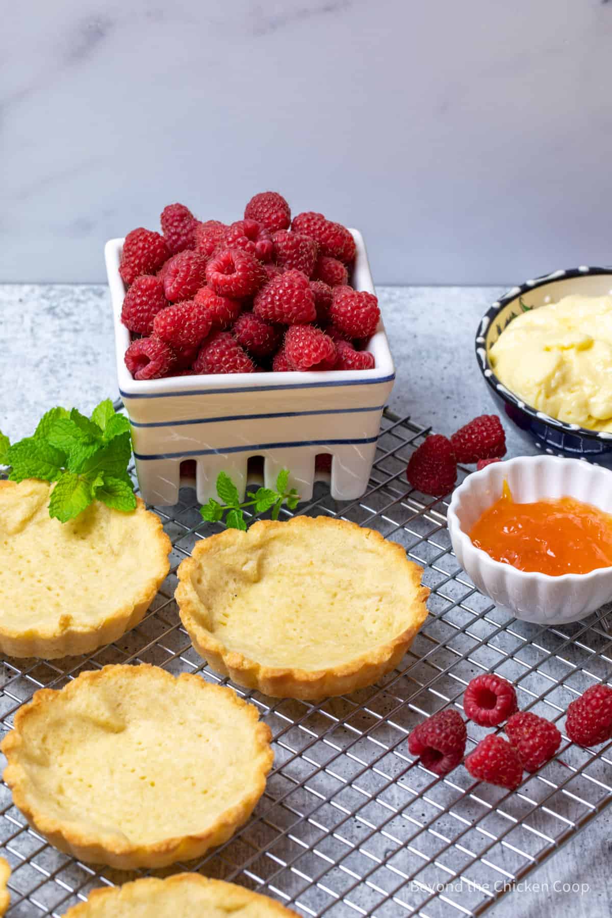 Mini tart shells on a baking rack with fresh raspberries. 