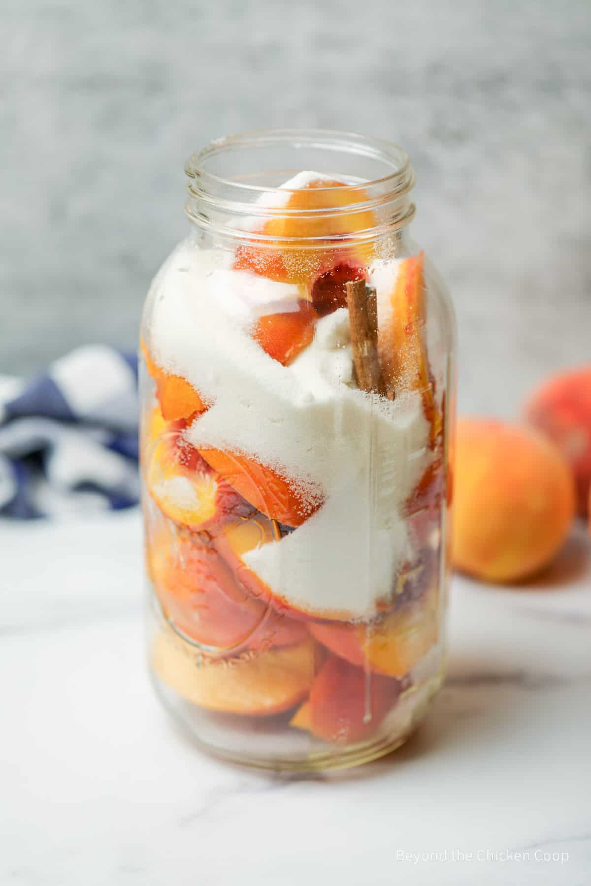 Sugar poured over peaches in a glass container. 