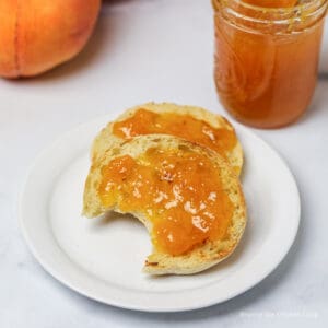 An English muffin covered with peach jam.