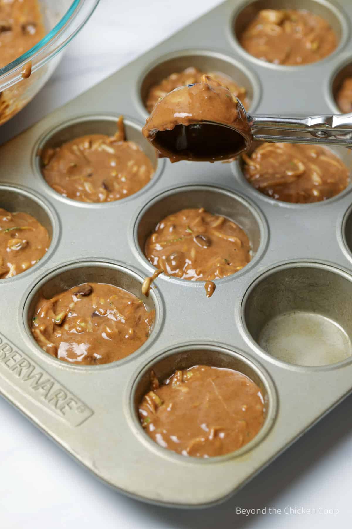 Adding muffin batter to a muffin tin.