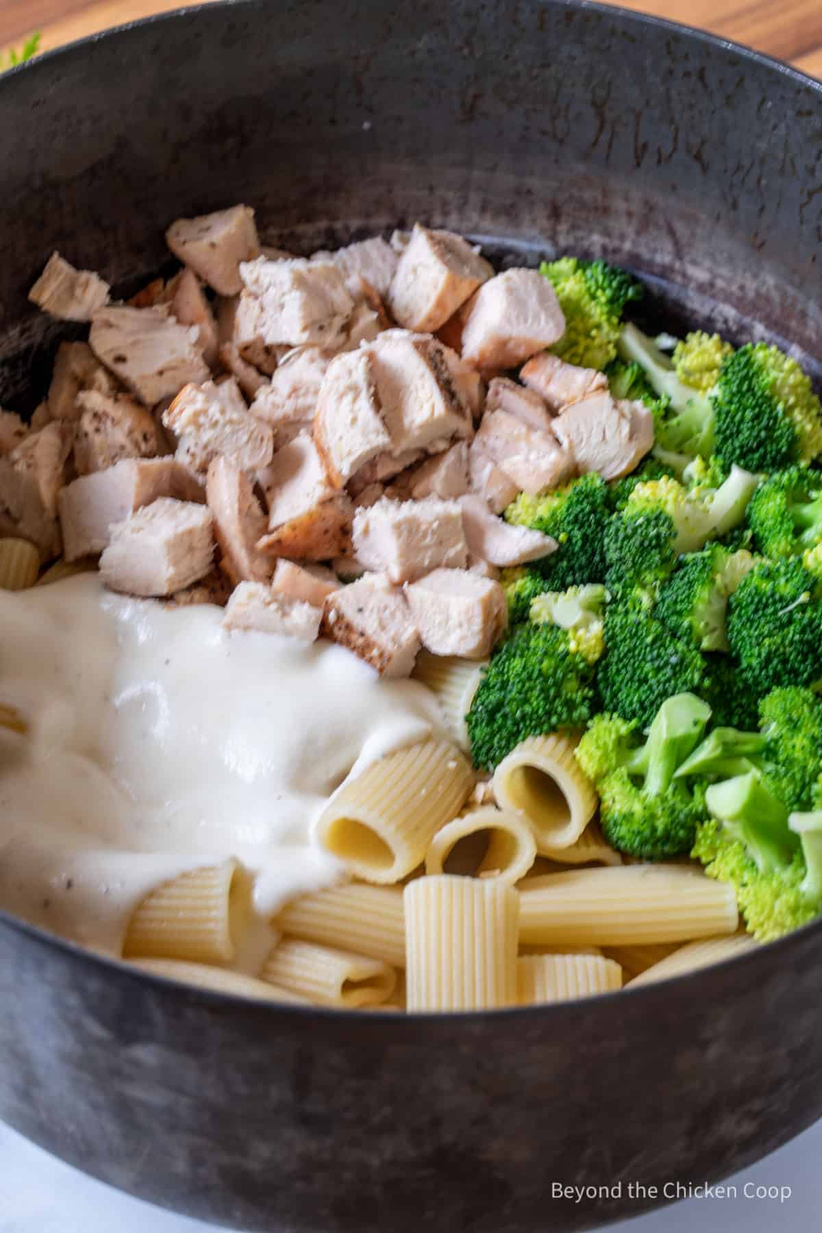 Chicken, broccoli, pasta and a creamy white sauce in a pot.