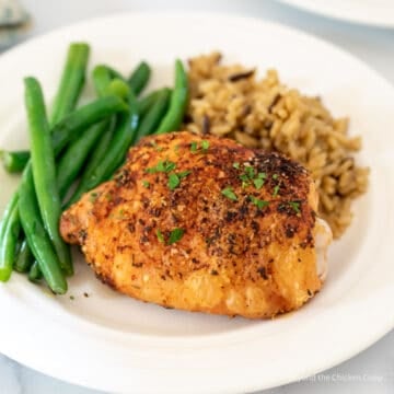 A baked chicken thigh on a plate with rice and green beans.