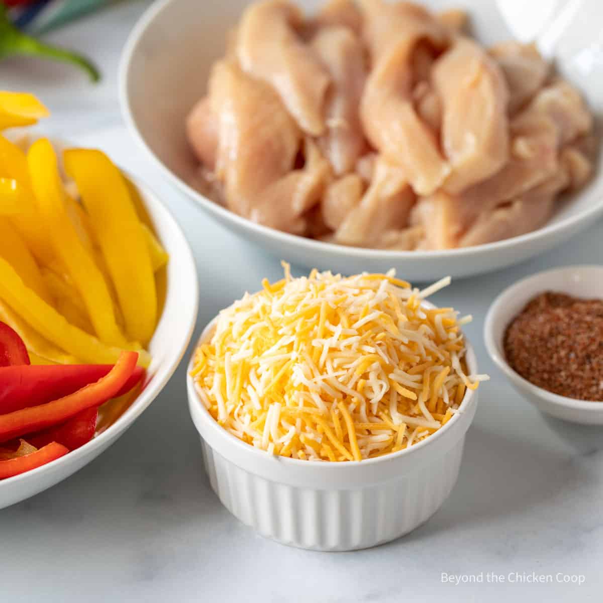 Bowls filled with sliced peppers, chicken, shredded cheese and fajita seasoning.
